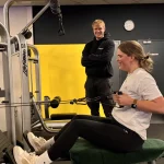 een jonge zwangere vrouw is veilig aan het trainen met een trekbelt onder begeleiding van een personal trainer