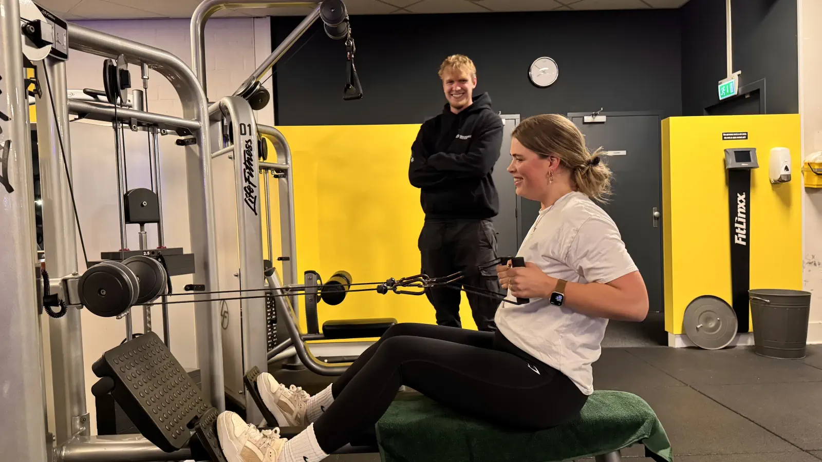 een jonge zwangere vrouw is veilig aan het trainen met een trekbelt onder begeleiding van een personal trainer